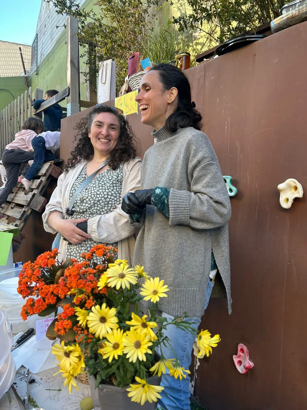 Dos madres de la AFA riendo junto a un ramo de flores en la fiesta de primavera